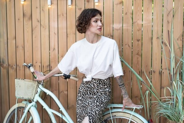 A stylish woman wearing a Shein graphic tee tucked into a high-waisted, pleated midi skirt. She's accessorized with delicate gold jewelry, including a layered necklace and hoop earrings. Her hair is styled in soft waves, and she's holding a structured handbag in a complementary color.