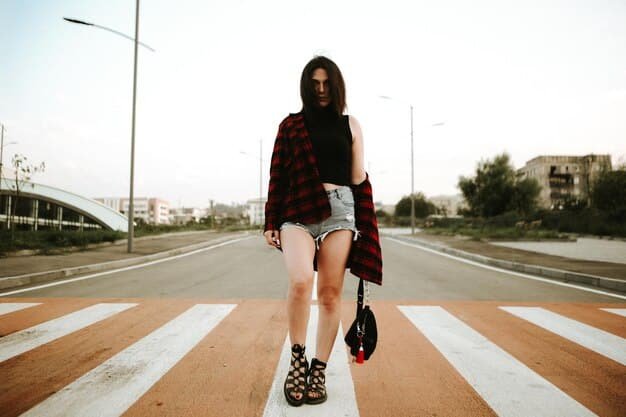 A street style shot capturing a woman in a plaid Shein mini skirt, paired with a vintage band t-shirt, fishnet stockings, and combat boots. She is also wearing a black leather jacket and round sunglasses, giving off a grunge and edgy vibe.