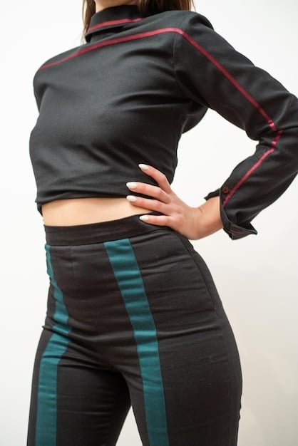 A close-up shot of a woman wearing high-waisted leggings (possibly black or navy blue) and a supportive sports bra in a matching color. She is in a well-lit gym, with various exercise equipment blurred in the background. The focus is on the fit and fabric of the athleisure wear. The leggings should have a pocket.