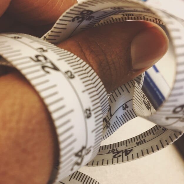 A close-up of a measuring tape accurately encircling a person's waist. The focus is on the placement of the tape measure and the clear reading of the measurement in inches.