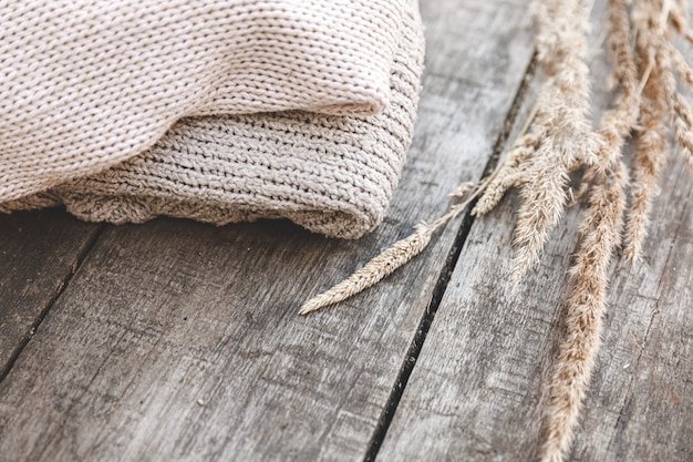 A close-up shot of various fabric textures, including cream-colored linen, white cotton knit, and a beige cable-knit sweater. The fabrics are arranged on a wooden table with natural light.