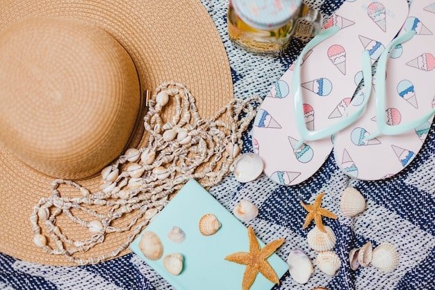 A flat lay of Coastal Grandmother accessories, including a straw hat, woven tote bag, delicate gold necklace, and beige leather sandals, arranged on a white linen background.