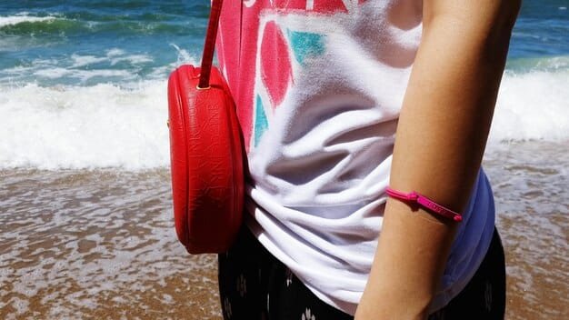 A close-up shot of a Shein fanny pack with a holographic design, showcasing its functionality and style, paired with sunglasses and a beaded bracelet on a festival-goer's wrist.