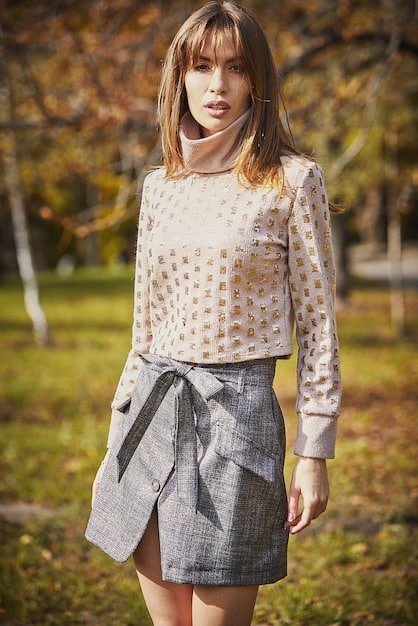 A woman wearing a polka dot blouse and a checkered skirt, standing in a well-lit studio. The polka dots are small and white, contrasted against a navy blue background. The checkered skirt is a classic gingham pattern in black and white. The woman is smiling confidently, with her hands on her hips.