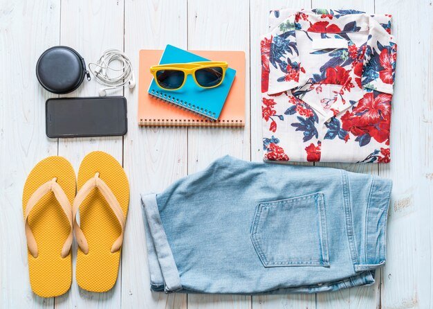 A flat lay showcasing three different Shein outfits for a vacation. The first outfit includes a floral crop top with high-waisted shorts; the second features a striped maxi dress with a wide-brimmed hat; and the third consists of a linen shirt with white capri pants. Each outfit demonstrates style versatility.