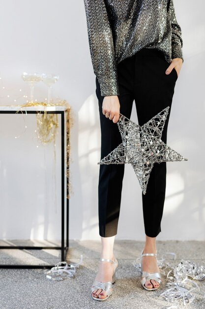 A close-up shot of a Shein outfit featuring a velvet blazer paired with a sequined camisole and black fitted trousers. The outfit is accessorized with a gold necklace and clutch. The background is a softly blurred holiday-themed setting.